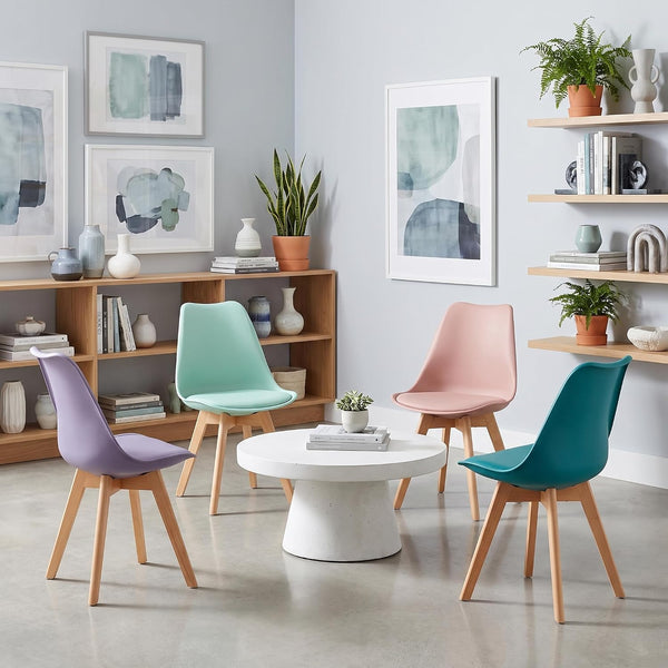 Four modern molded plastic chairs in lavender, mint green, blush pink, and teal, arranged around a round white coffee table in a styled living room setting.